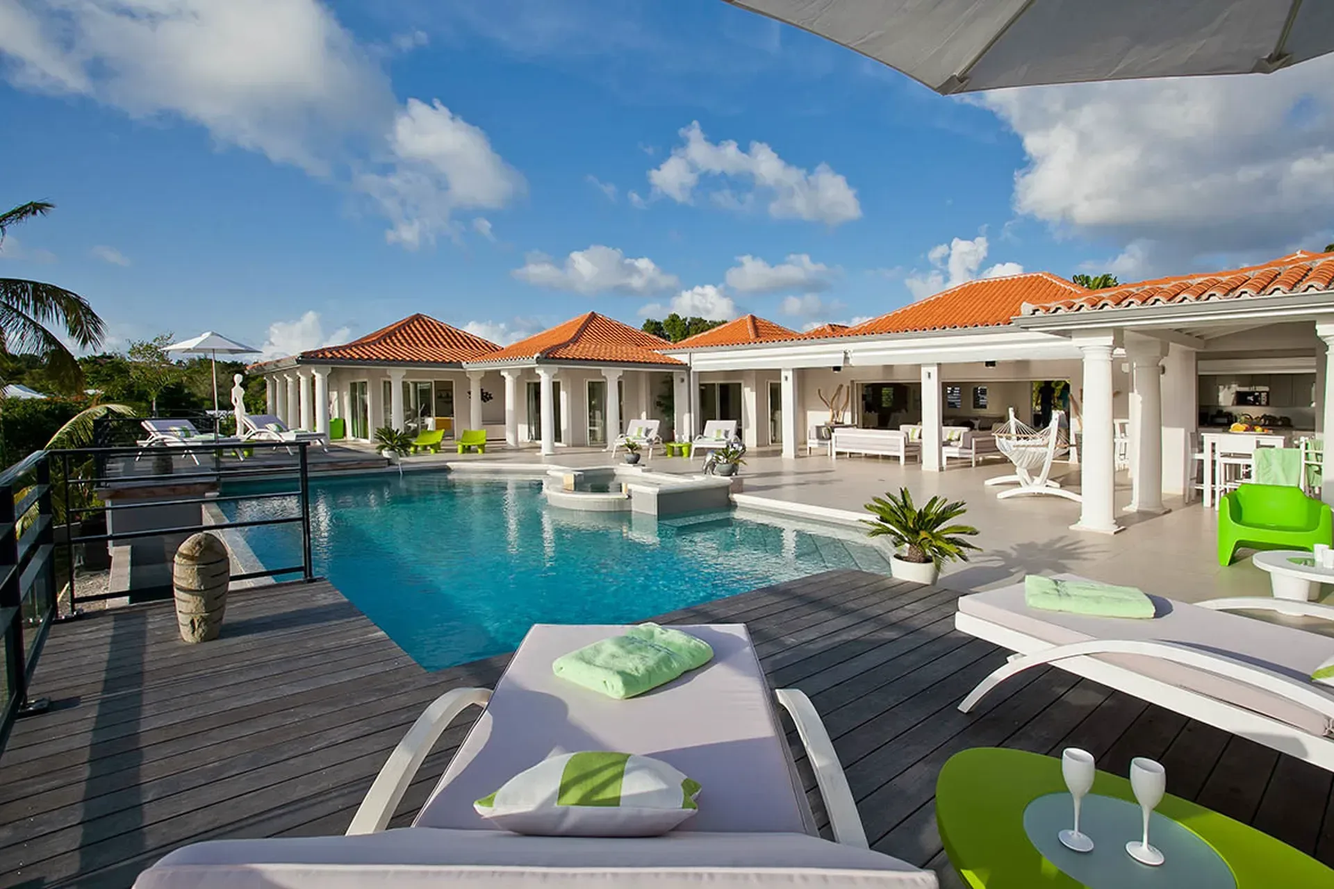 Pool area with wooden deck and Mediterranean-style villa.