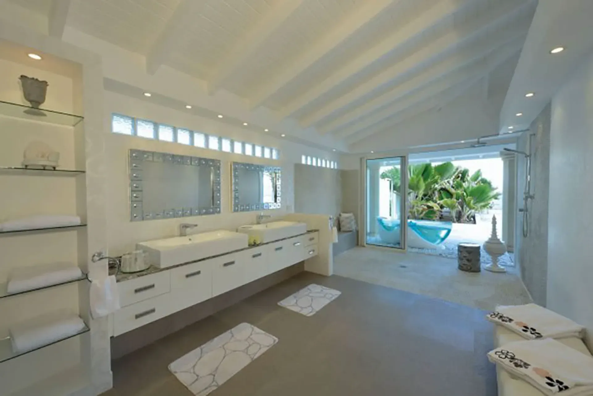 A spa-inspired bathroom with dual vessel sinks, vaulted ceilings, and tropical views through sliding doors.