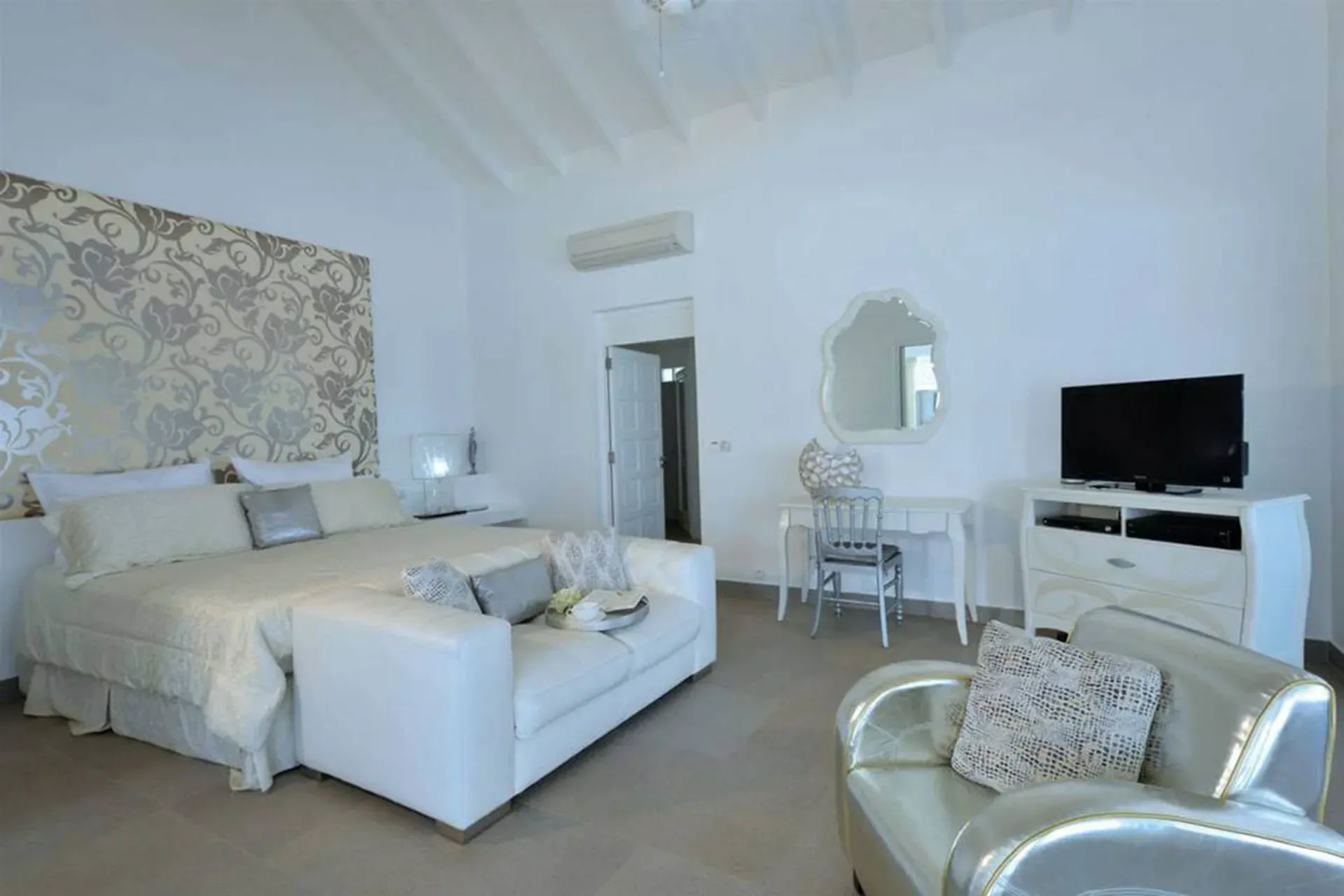 A serene retreat with an ornate floral headboard, white sofa, and elegant silver accents under soaring vaulted ceilings.