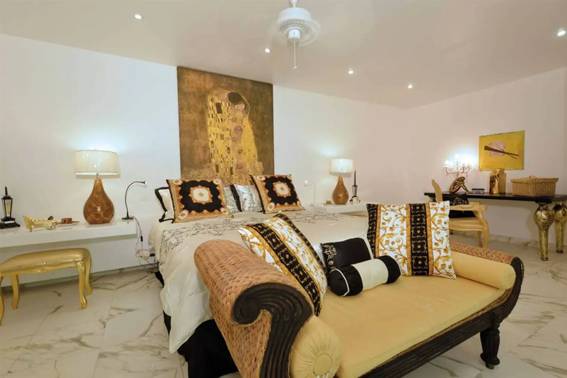 A dramatic master suite featuring Gustav Klimt's "The Kiss" as a headboard, gold accents, and a vibrant yellow chaise.