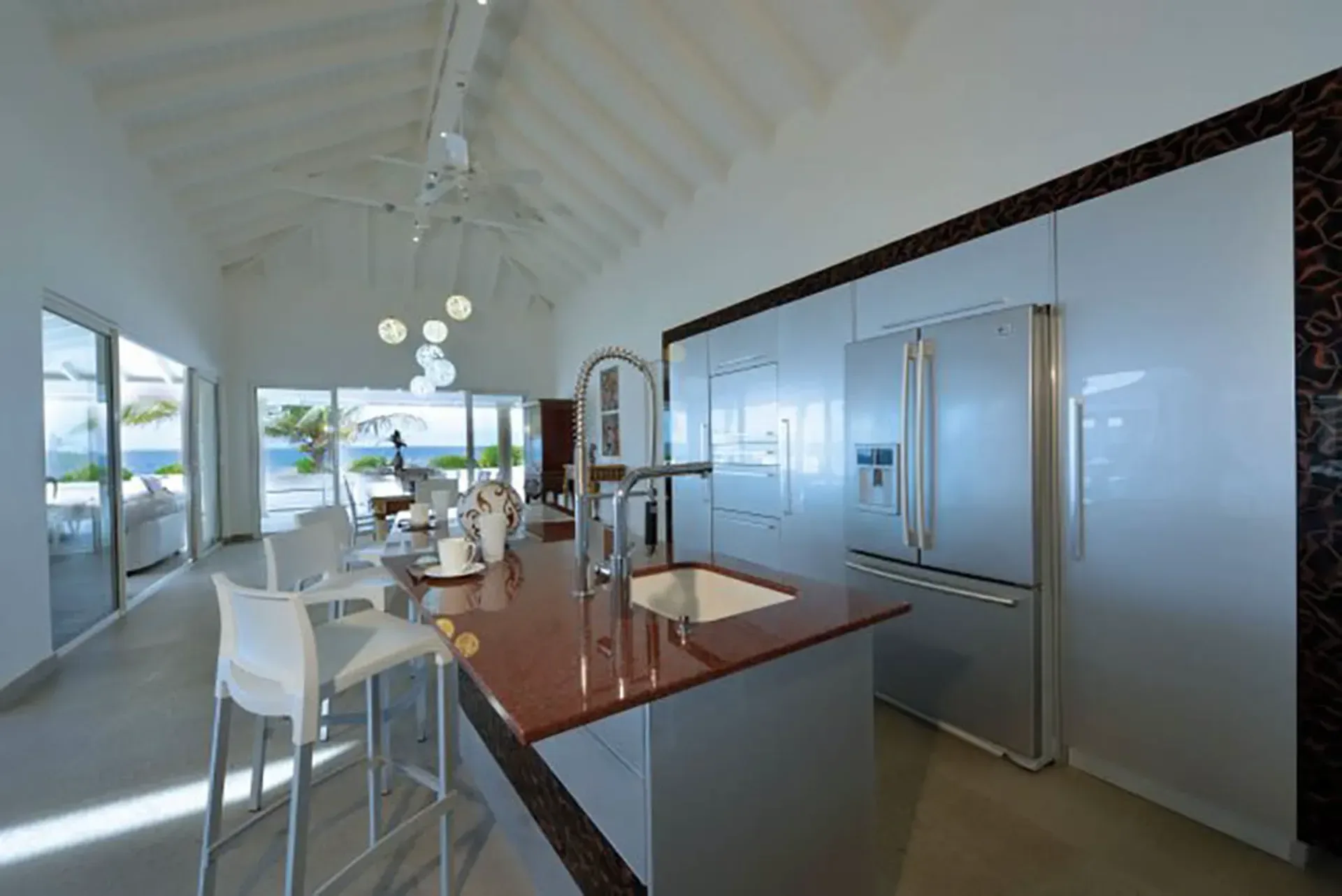 A chef's kitchen with dark granite island, stainless appliances, and direct beach views through sliding glass doors.