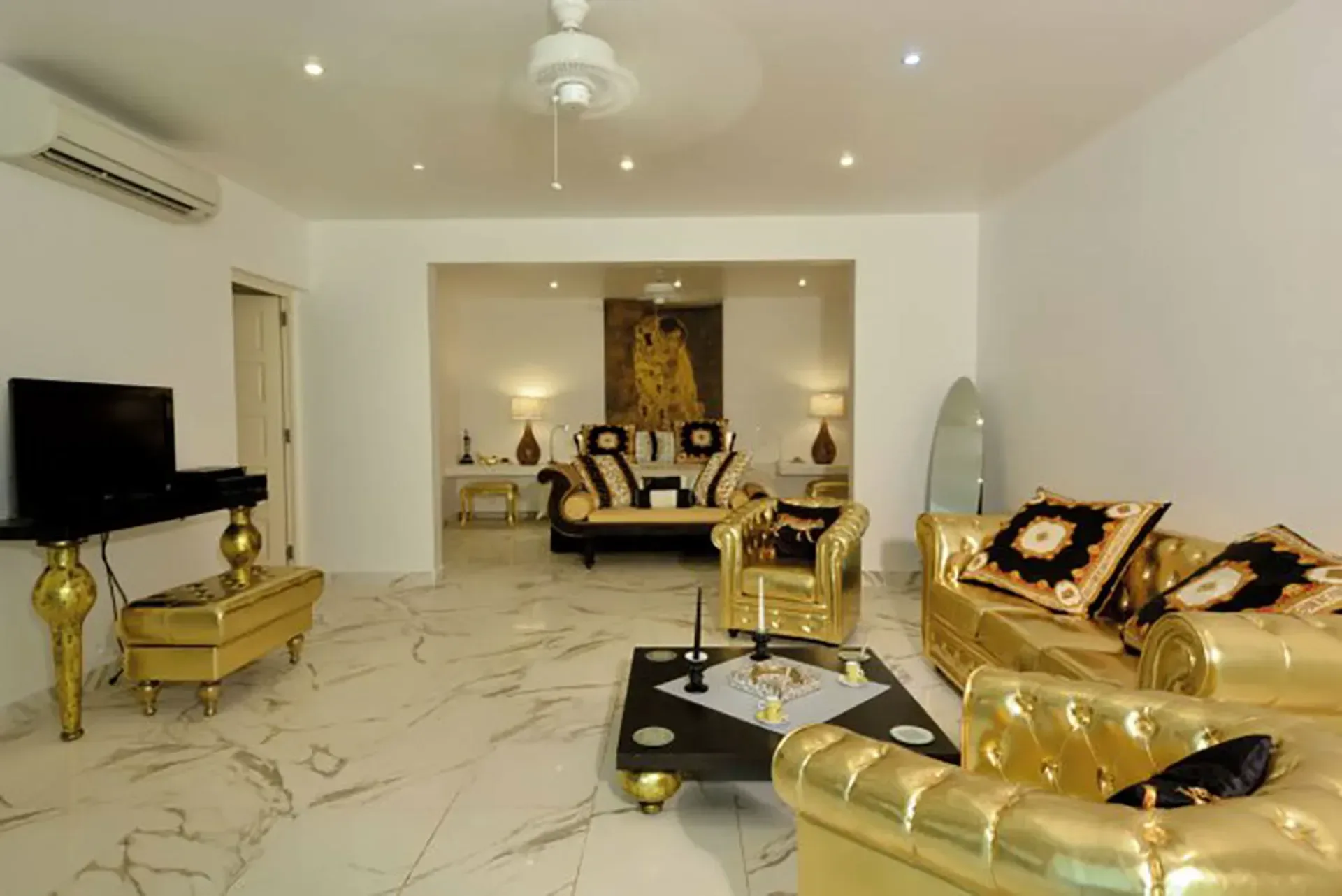 Luxurious living room with opulent gold-upholstered seating, marble floors, and elegant black and gold coffee tables.