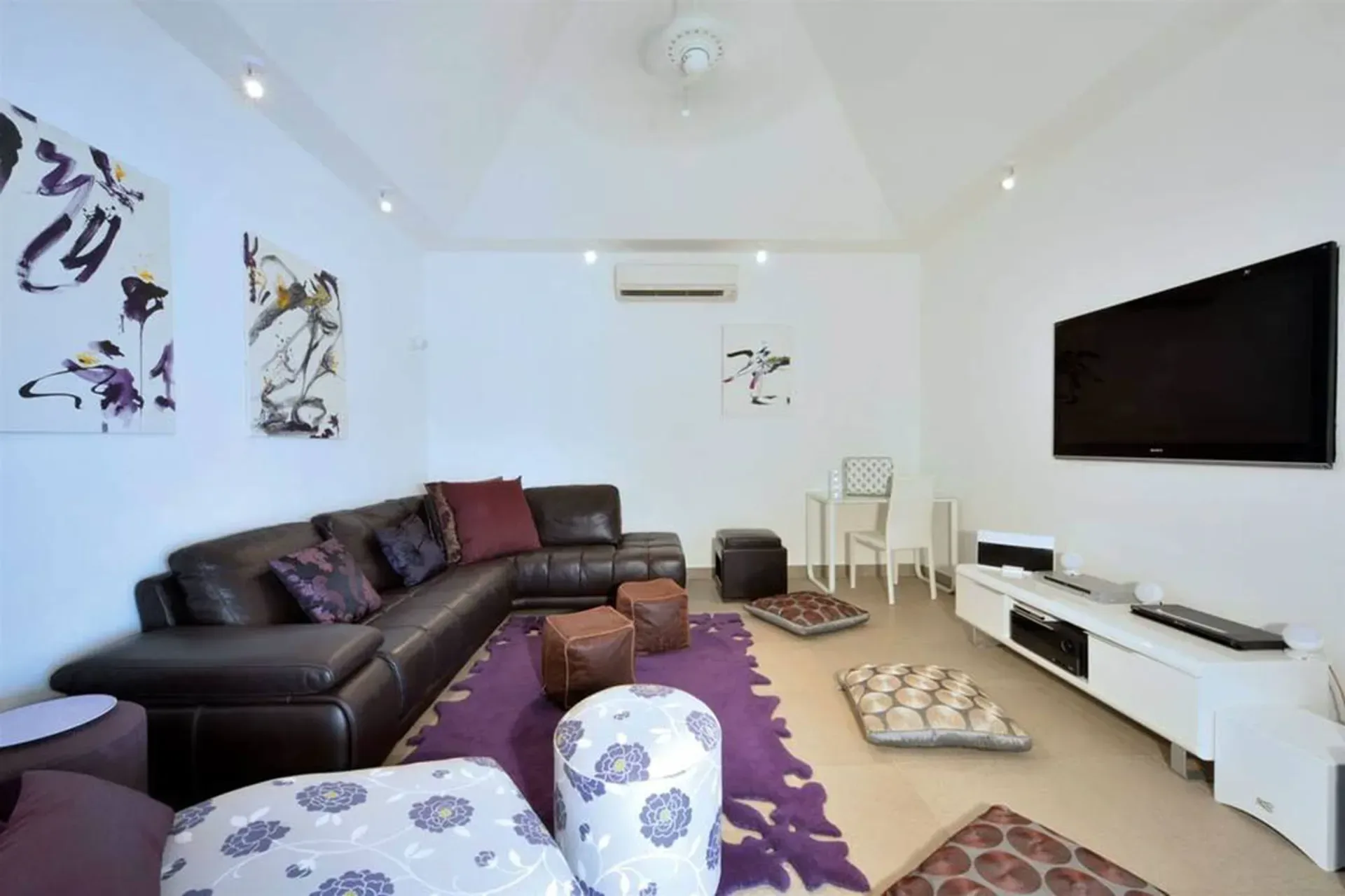 Cozy movie nights in the media room with plush leather sectional, wall-mounted TV, and colorful floor cushions.