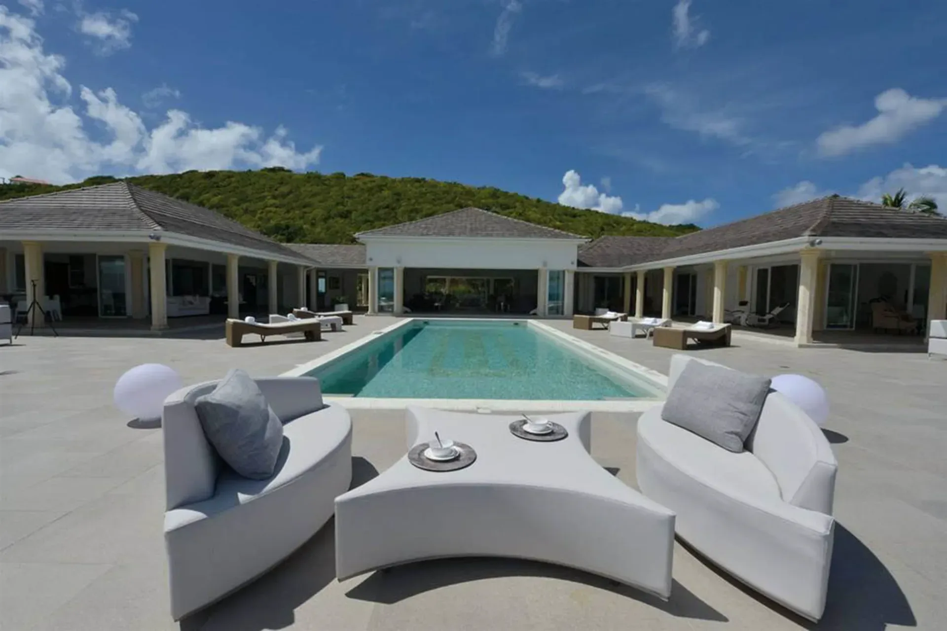 Entertain on your pool terrace with curved white seating, comfortable loungers, and lush hillside views.