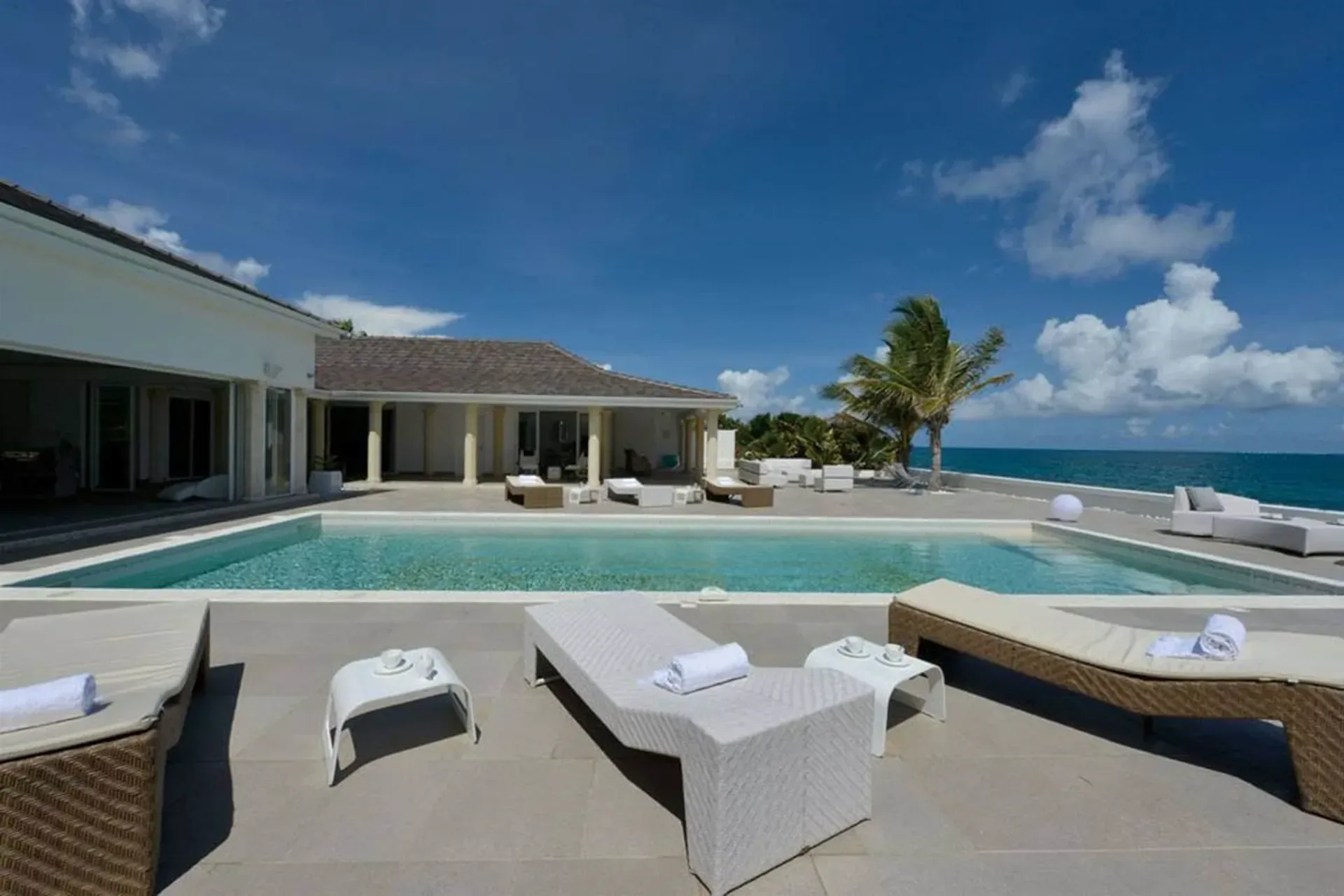 Relax on a stunning infinity pool terrace with comfortable loungers, swaying palms, and breathtaking ocean views from your private Caribbean retreat.