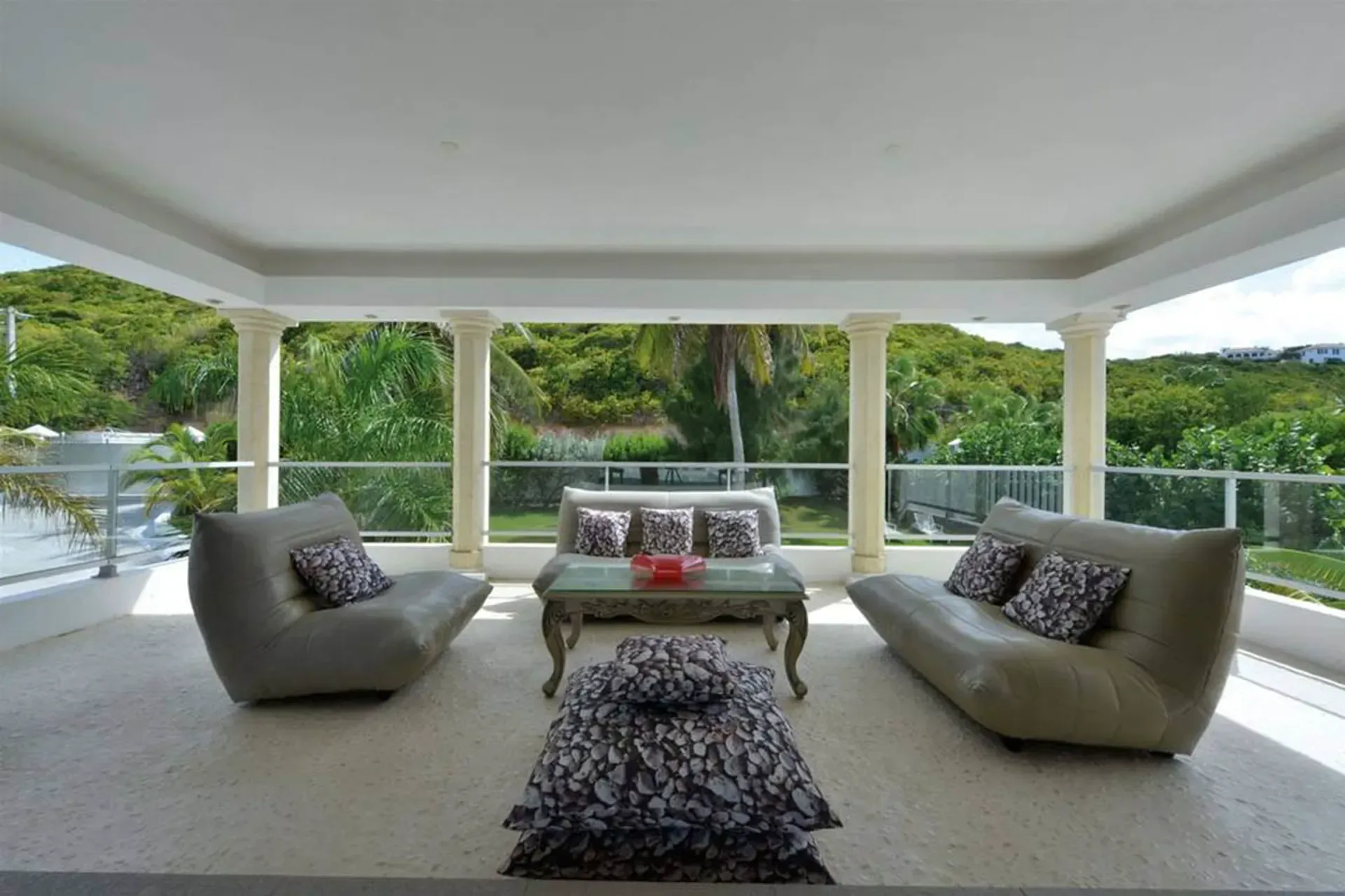 Relax on comfortable grey sofas with tropical hillside views from your covered terrace with classical columns.