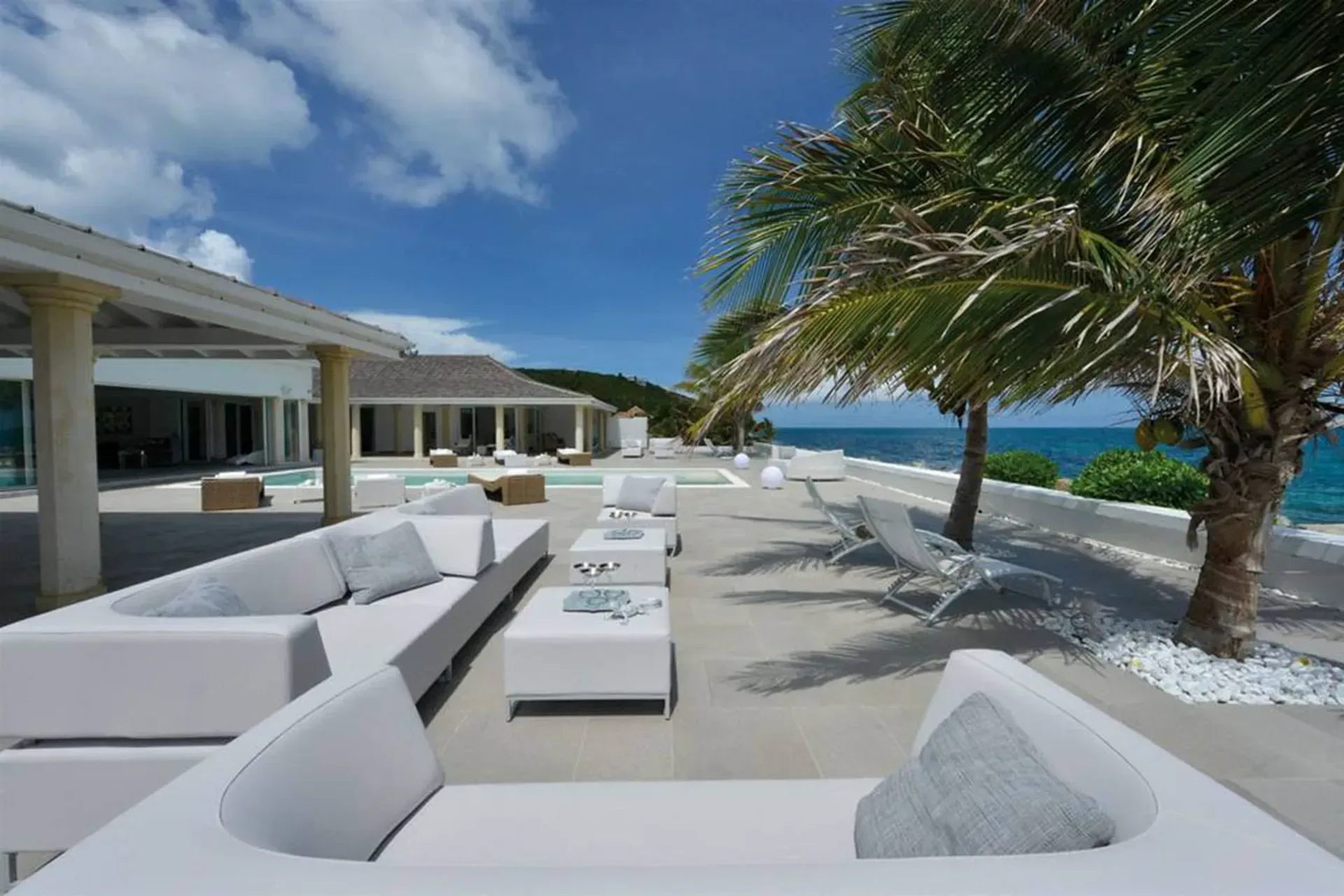 Relax on modern white sectionals by the infinity pool with swaying palms and endless ocean views.