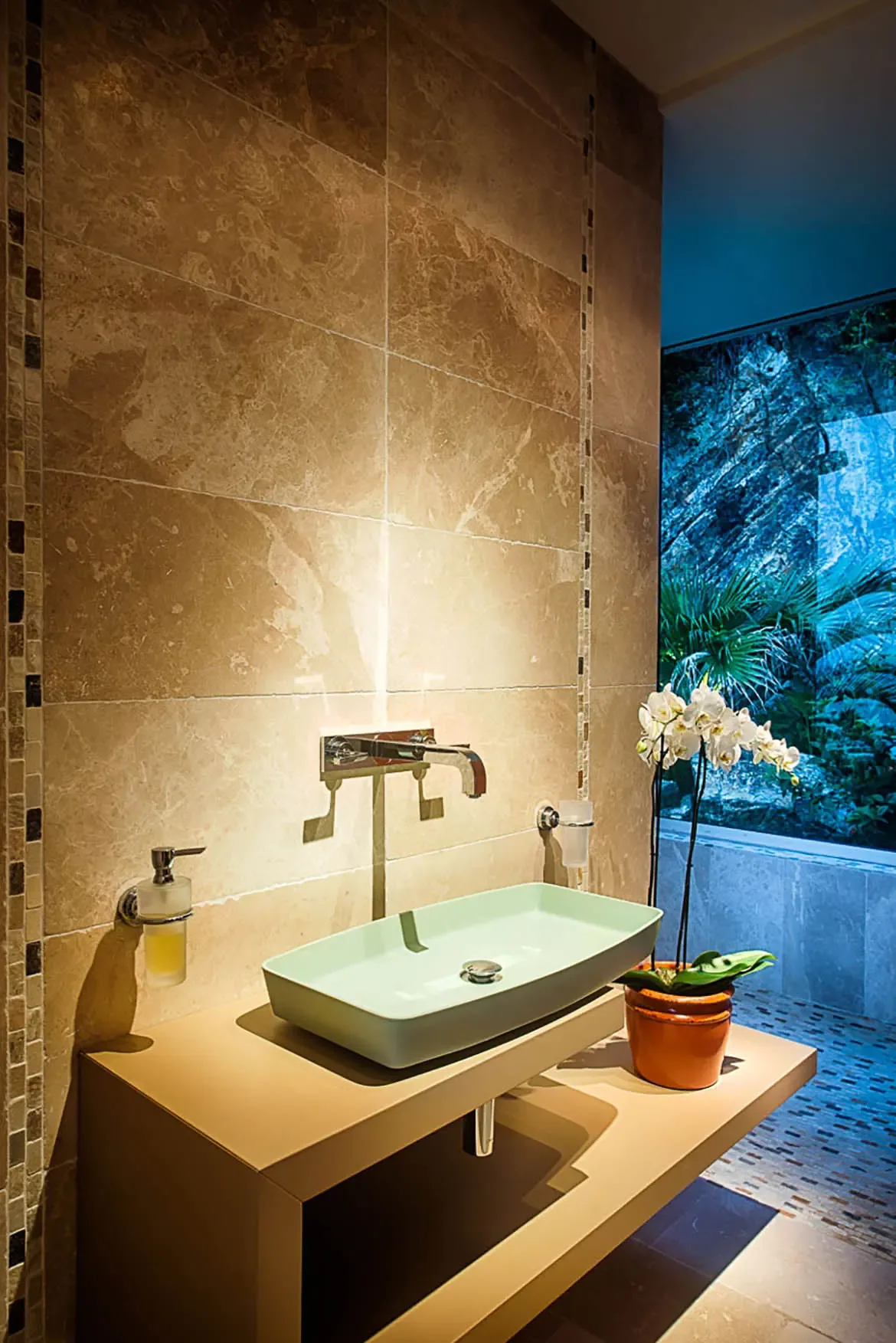 A modern bathroom vanity with light green rectangular vessel sink, minimalist floating shelf, white orchid, and large window offering vibrant tropical views.