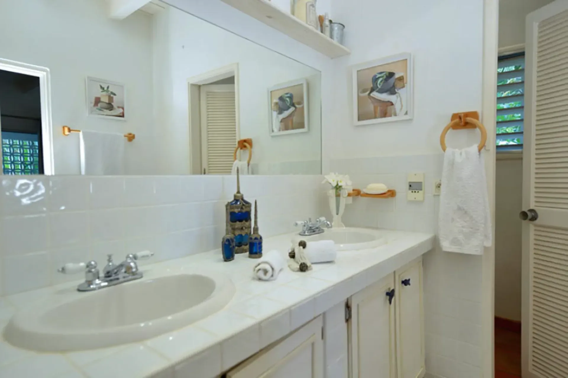 A functional bathroom with double vanity, large mirror, and classic Caribbean louvered doors.