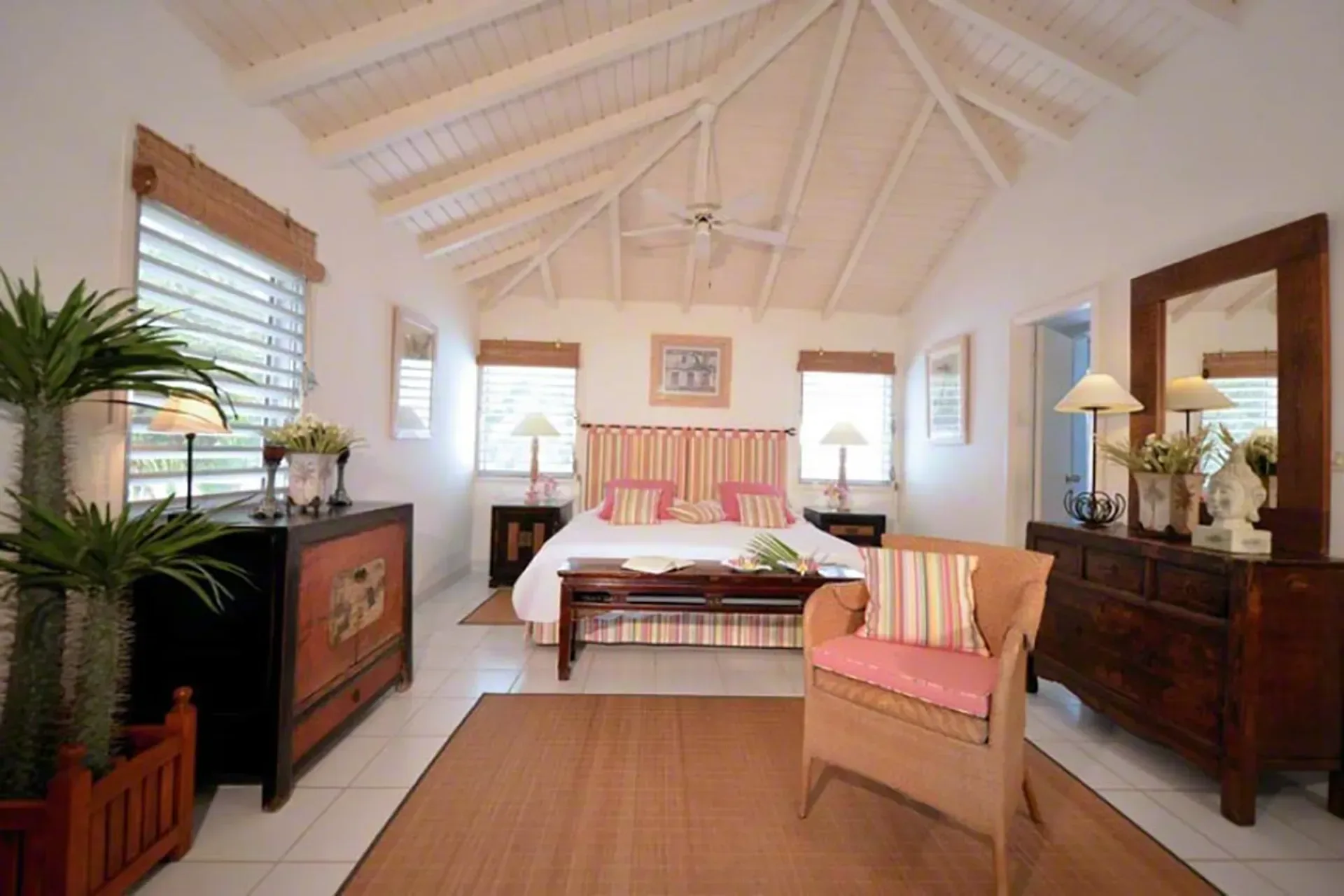 A spacious bedroom with colorful striped headboard, vaulted ceilings, and tropical accents.