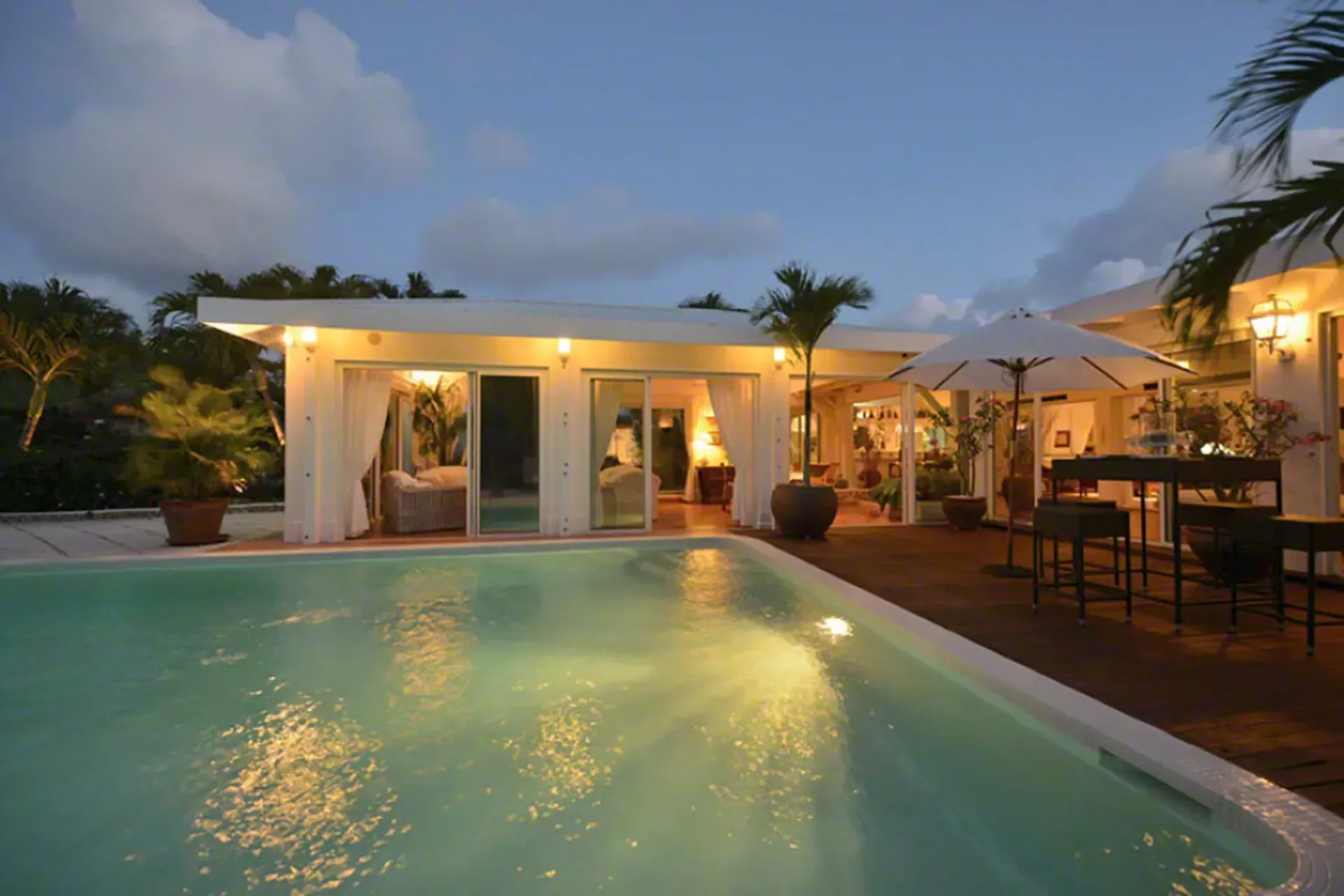 Your illuminated pool terrace at dusk with outdoor dining and warm evening ambiance.