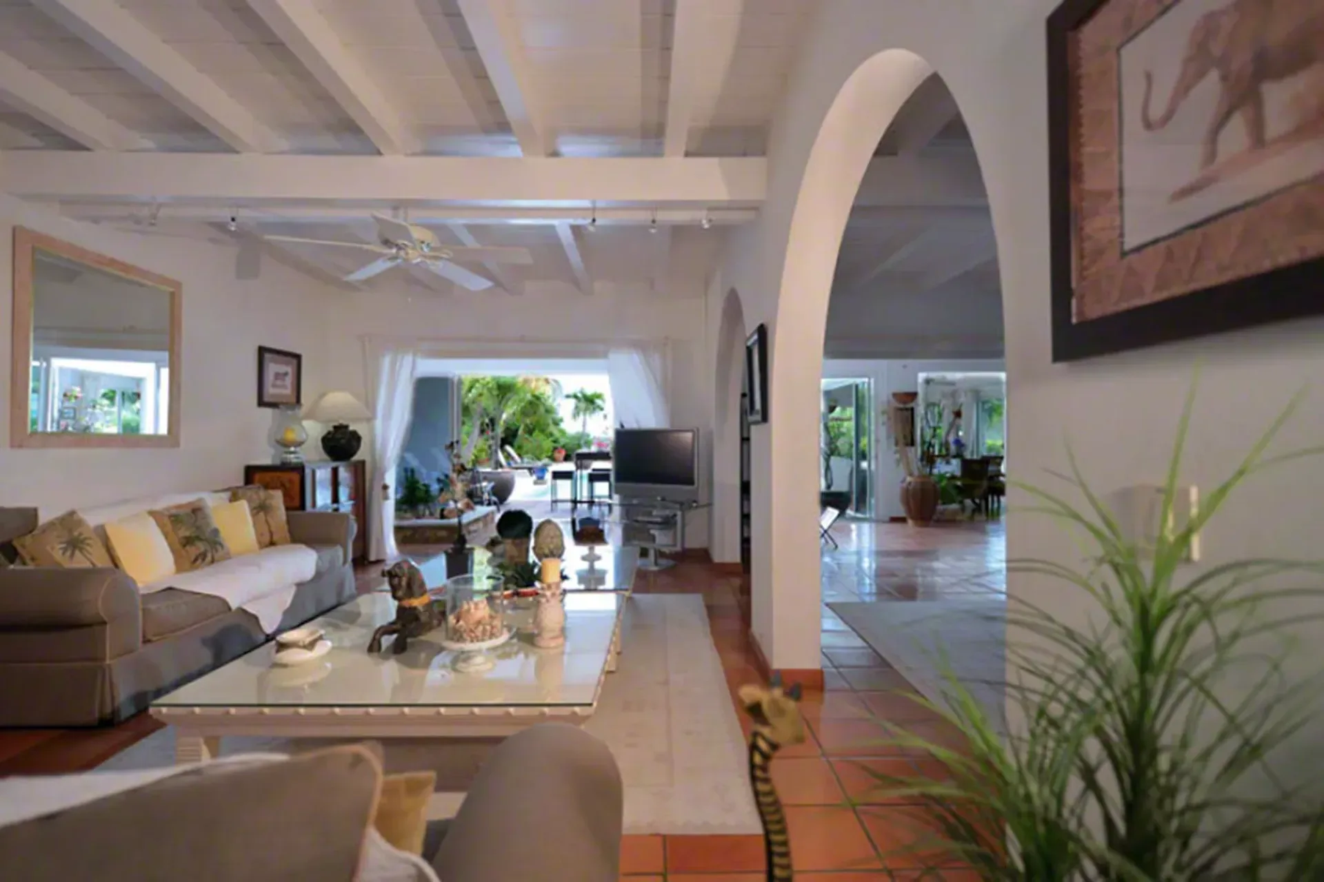 An airy living room with beamed ceilings, terracotta tiles, and open doors to the terrace.