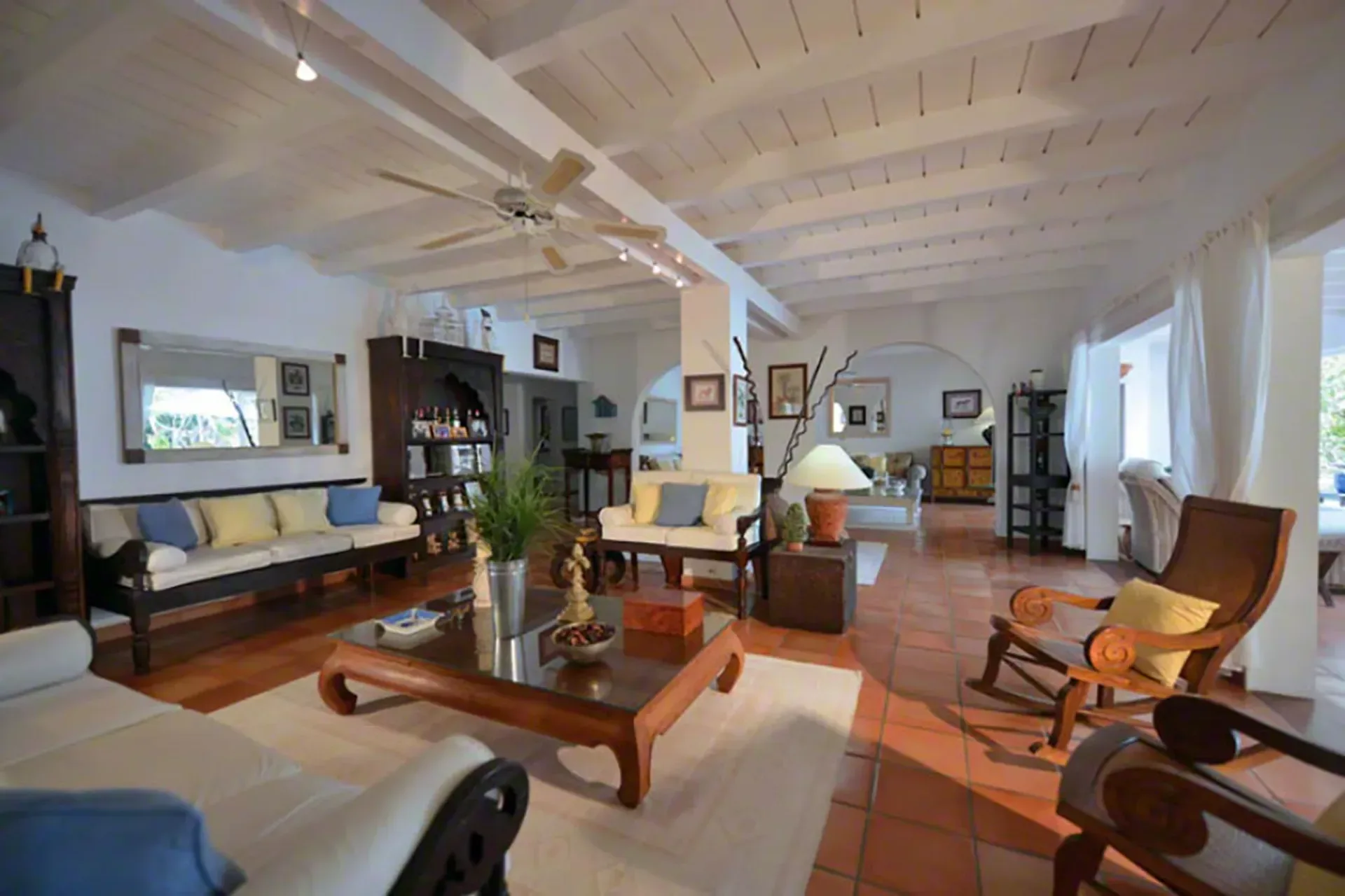 A welcoming living room with terracotta floors, wood furniture, and tropical prints.