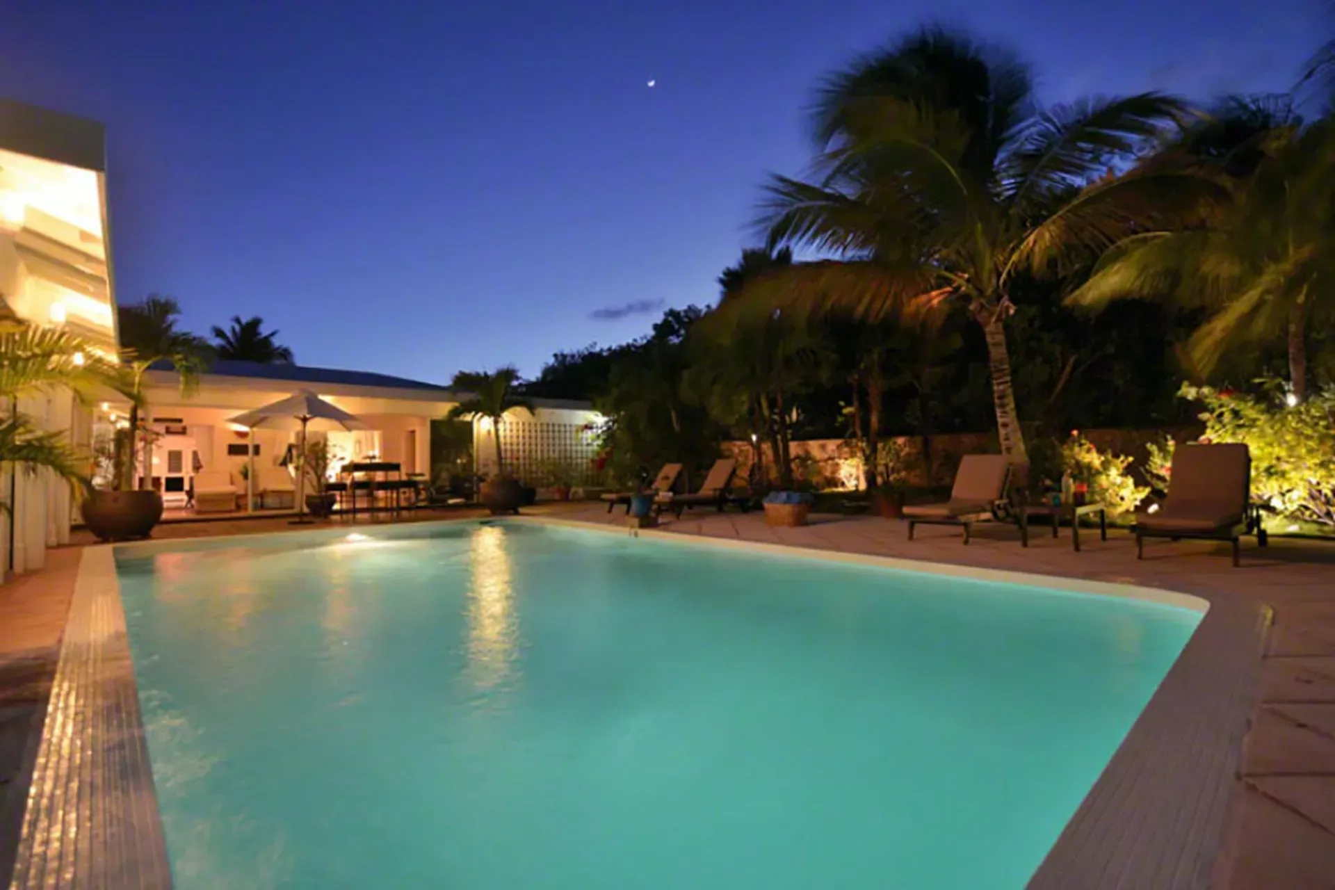 Evening swim under the stars with illuminated pool and warm villa lighting.