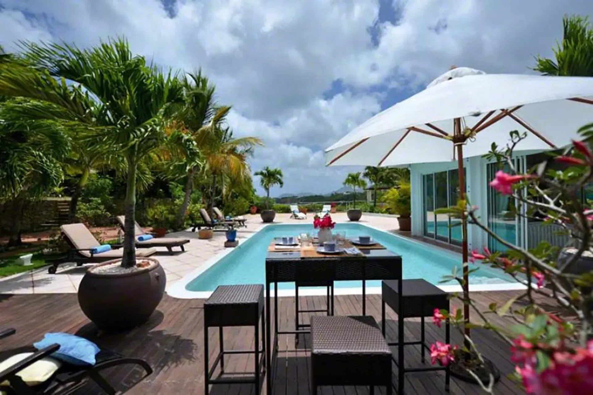 Outdoor dining by the pool with wicker furniture and tropical landscaping.